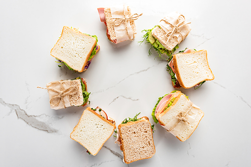 top view of fresh sandwiches arranged in round frame on marble white surface