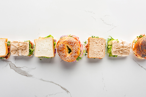 flat lay with fresh sandwiches and bagel on marble white surface