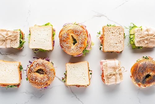 flat lay with fresh sandwiches and bagels on marble white surface
