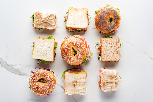 flat lay with fresh sandwiches and bagels on marble white surface