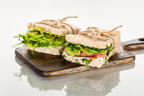 fresh green sandwiches with avocado and meat on wooden cutting board on white surface