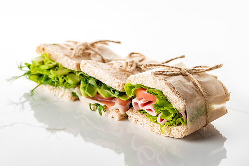 selective focus of fresh green sandwiches with avocado and meat on white surface
