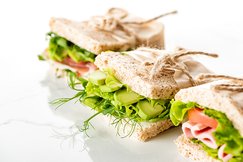 selective focus of fresh green sandwiches with avocado and meat on white surface