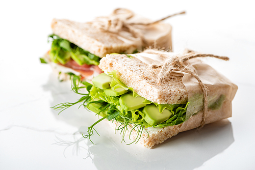 selective focus of fresh green sandwiches with avocado on marble white surface
