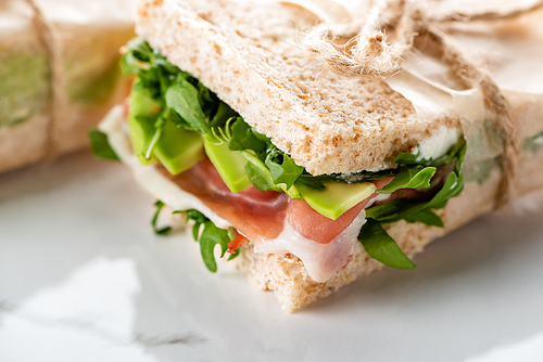 close up view of fresh green sandwich with jamon on marble white surface