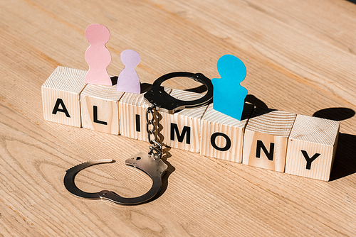 wooden blocks with alimony lettering near family paper cut and handcuffs on surface