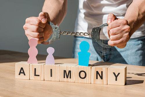 cropped view of handcuffed man near wooden blocks with alimony lettering and paper people