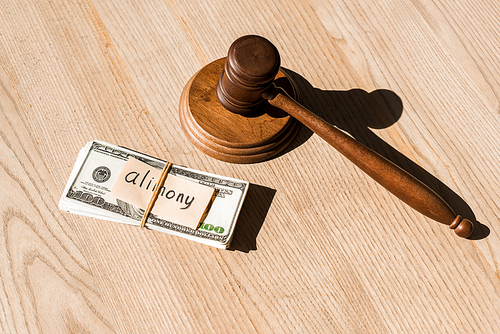 wooden gavel near dollar banknotes and paper with alimony lettering on table