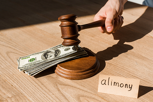 cropped view of judge holding gavel near dollar banknotes and paper with alimony lettering on desk