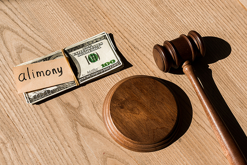 top view of gavel near dollar banknotes and paper with alimony lettering on wooden desk