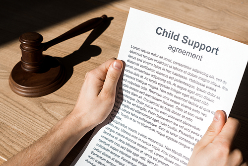 cropped view of man holding document with child support agreement near wooden gavel