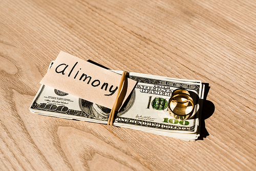 paper with alimony lettering on dollar banknotes near engagement rings