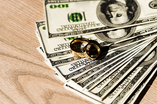 dollar banknotes near golden engagement rings on wooden surface