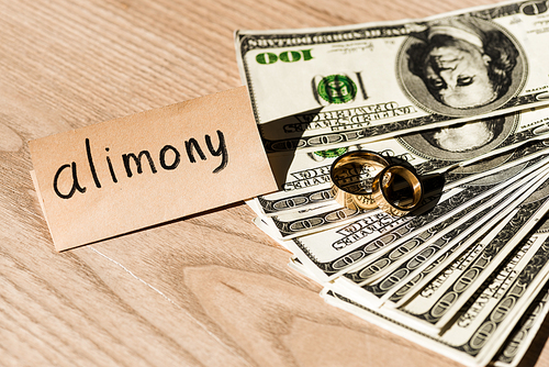 paper with alimony lettering near dollar banknotes and engagement rings