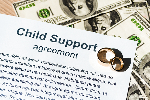 document with child support agreement near dollar banknotes and engagement rings