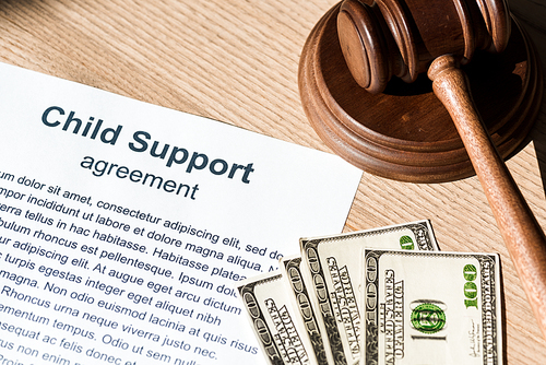 wooden gavel near document with child support agreement and dollar banknotes