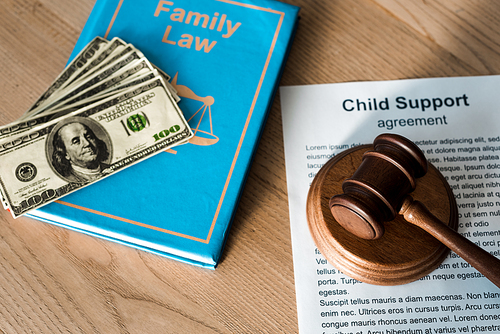 wooden gavel near document with child support agreement, dollar banknotes and family law
