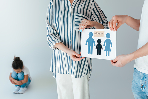 selective focus of parents holding paper with drawn family and alimony lettering near upset african american daughter on white