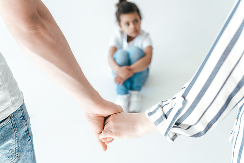 selective focus of foster parents holding hands near african american adopted daughter on white