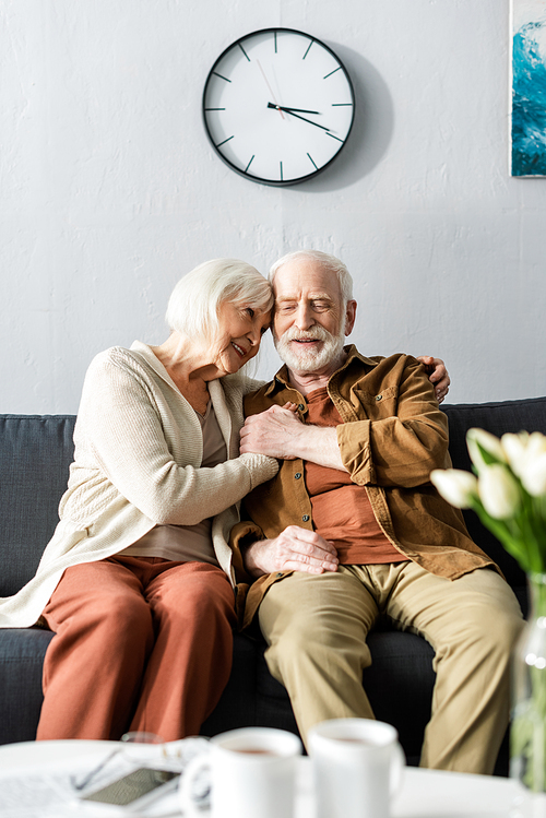 selective focus of happy senior couple sitting on sofa and holding hands