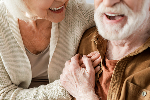 cropped view of laughing senior couple holding hands, selective focus