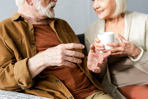 selective focus of senior man gesturing while talking to smiling wife holding cup of tea