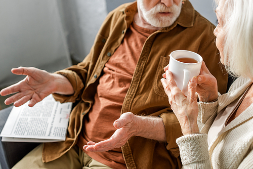 cropped view of senior man showing shrug gesture while talking to woman holding cup of tea