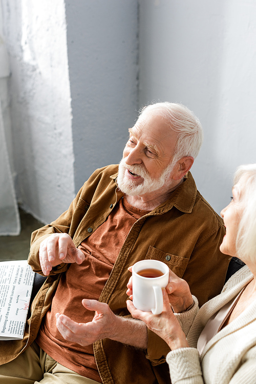 high angle view of smiling senior man talking to wife holding cup of tea