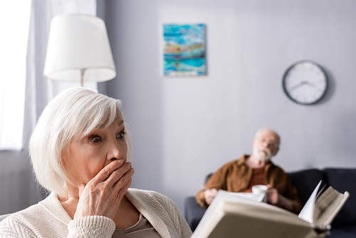 selective focus of senior man looking at shocked wife reading book