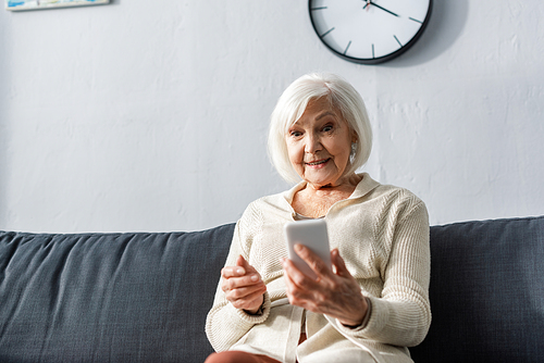 senior woman smiling while sitting on sofa and using smartphone