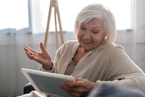 selective focus of cheerful senior woman sitting with open arm while using digital tablet