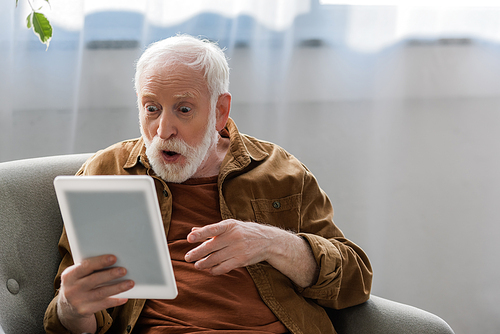 shocked senior man pointing with finger while using digital tablet
