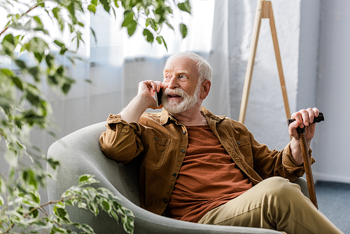 selective focus of happy senior man sitting in armchair and talking on smartphone