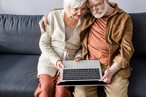 high angle view of happy senior couple sitting on sofa and using laptop