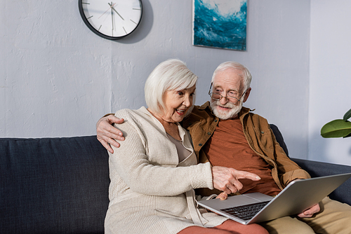 senior man hugging excited wife pointing with finger at laptop