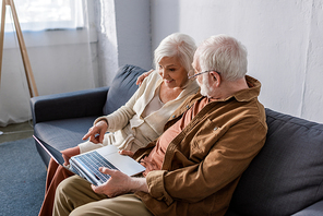 happy senior couple sitting on sofa and using laptop with blank screen