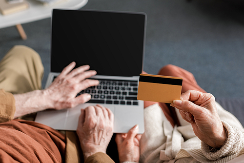 cropped view of senior man using aptop with blank screen near wife holding credit card, top view