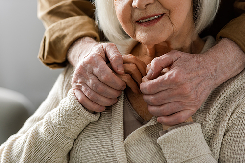 partial view of senior man holding hands of smiling wife