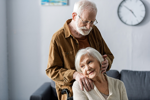 smiling senior woman sitting in . while husband holding hand on her shoulder and touching hair