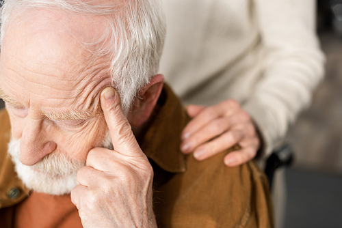 cropped view of woman touching shoulder of husband, sick on dementia, sitting with closed eyes and touching head