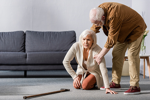senior man helping wife sitting on floor near walking stick