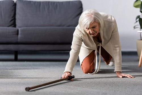 fallen, helpless senior woman trying to get walking stick on floor