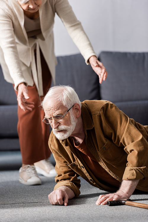 cropped view of woman helping fallen senior husband to get up from floor