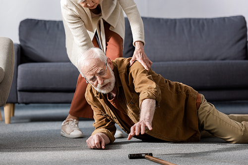 senior man lying on floor and trying to get walking stick while wife helping him