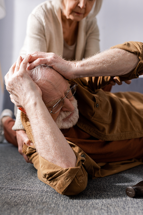 cropped view of senior woman near husband lying on floor and touching head