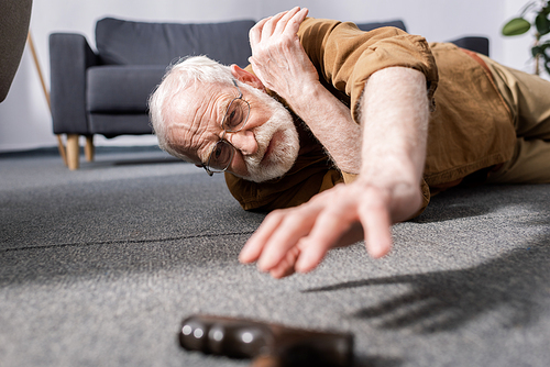 selective focus of helpless senior man fallen on floor and trying to get walking stick