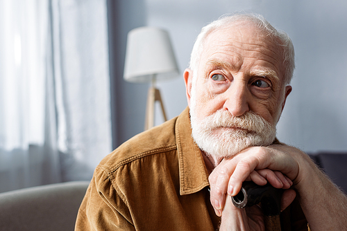 senior, lonely man looking away while sitting and leaning on walking stick