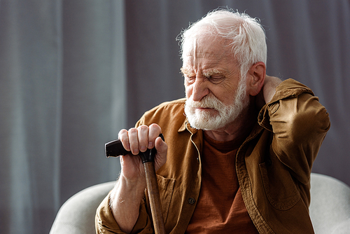 lonely senior man sitting with closed eyes, touching neck and holding walking stick