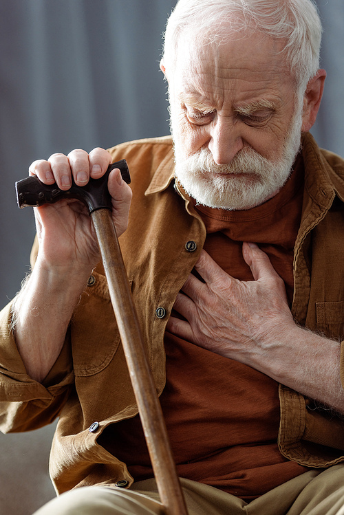 lonely senior man sitting with walking stick and touching chest while feeling bad
