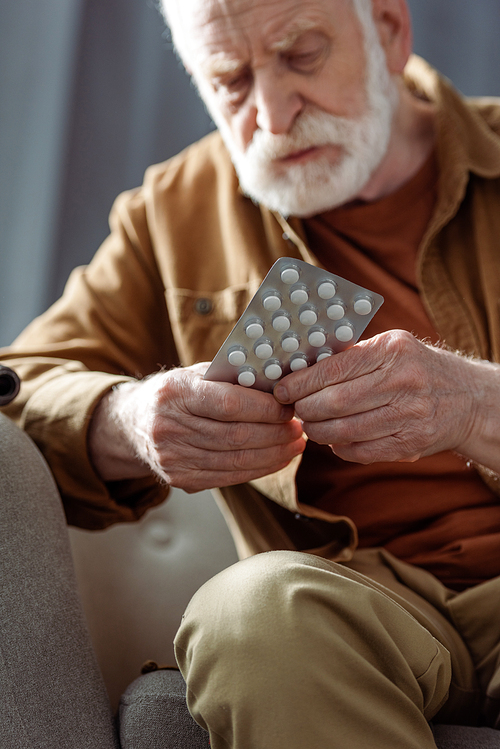 selective focus of lonely senior man feeling bad and holding pills